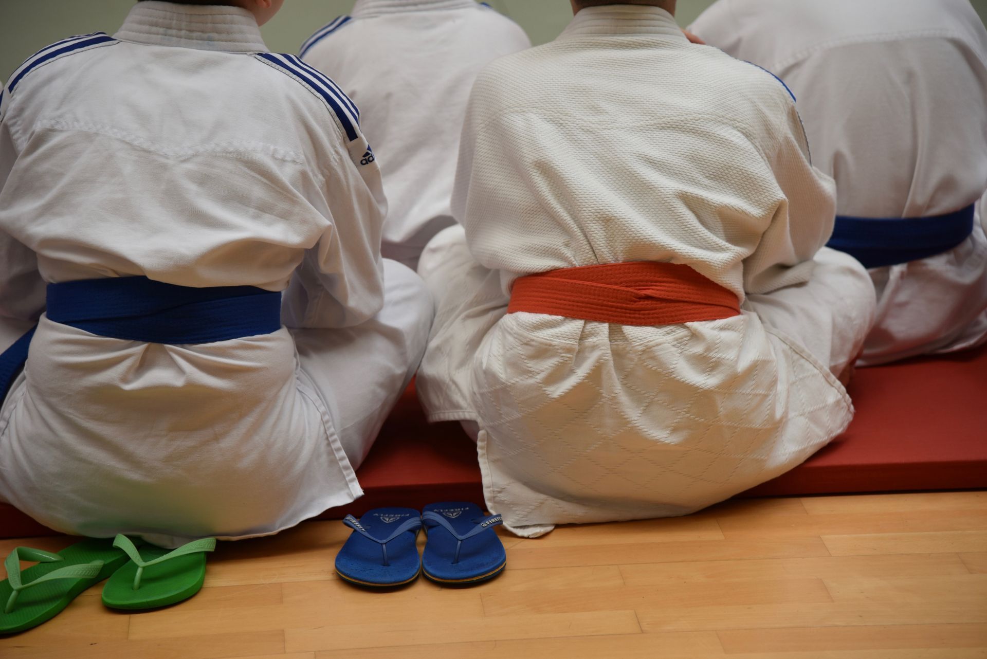 Martial arts instructor in black uniform instructs children in white gi, on a red mat
