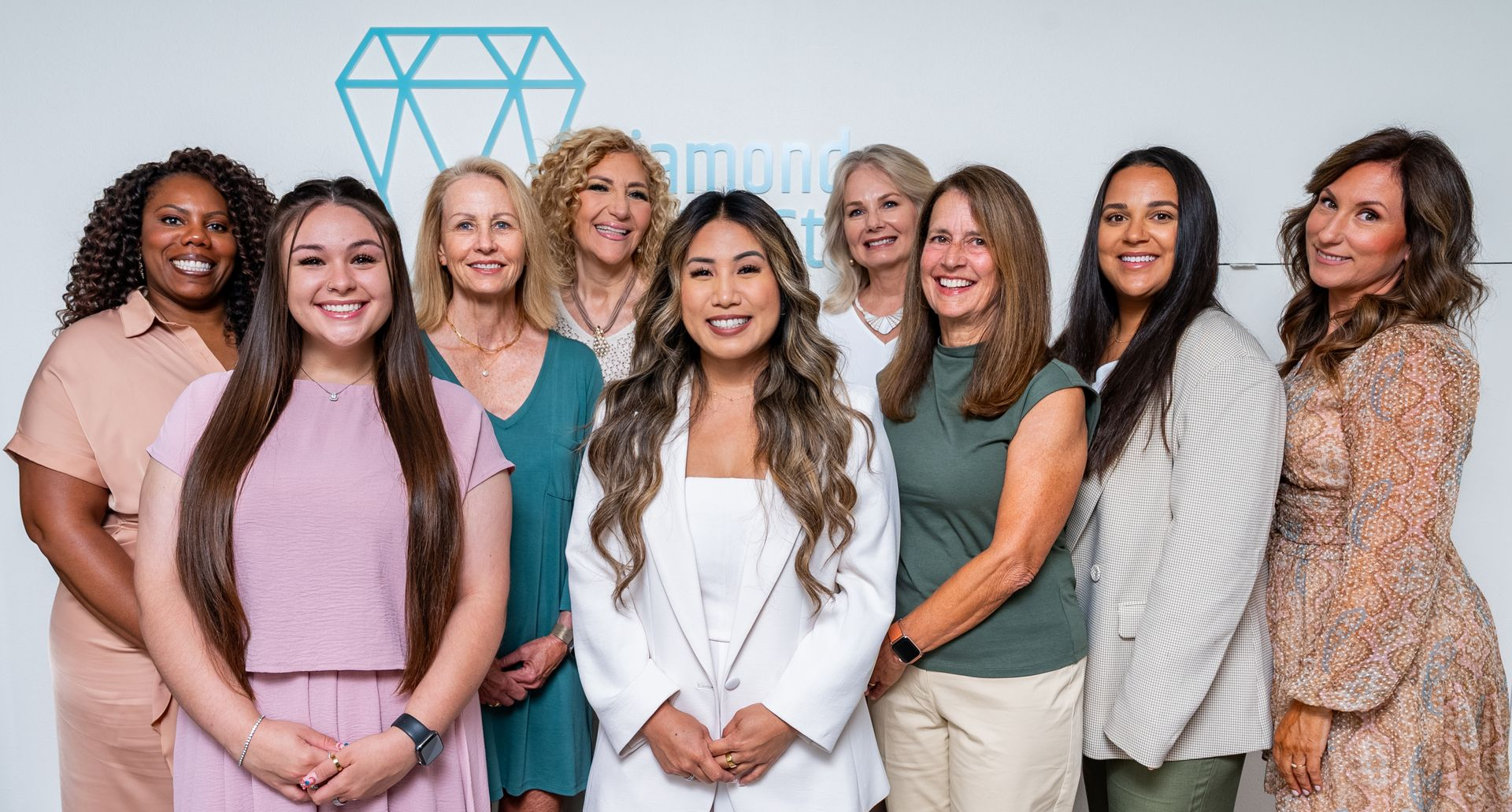 Group of diverse women posing in front of a diamond logo on a white backdrop.