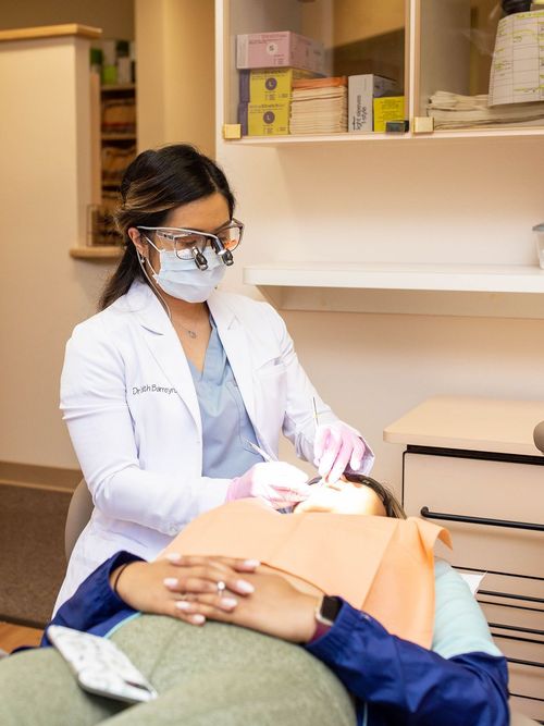 Dentist in mask and glasses examining patient's teeth in dental office.