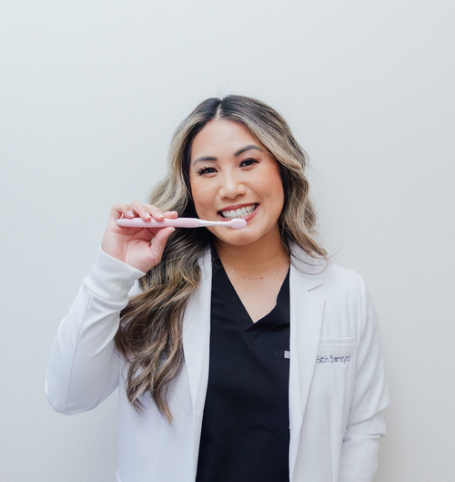 Woman in lab coat brushes her teeth, smiling.