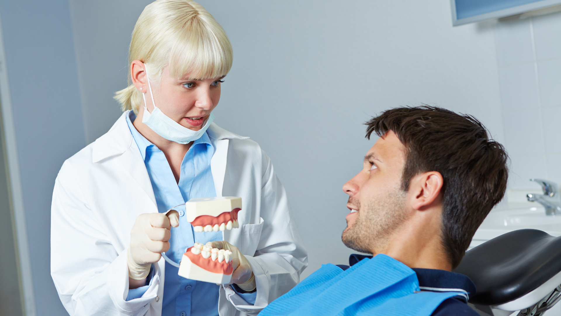 Dentist showing dental model to male patient, in a clinic setting.