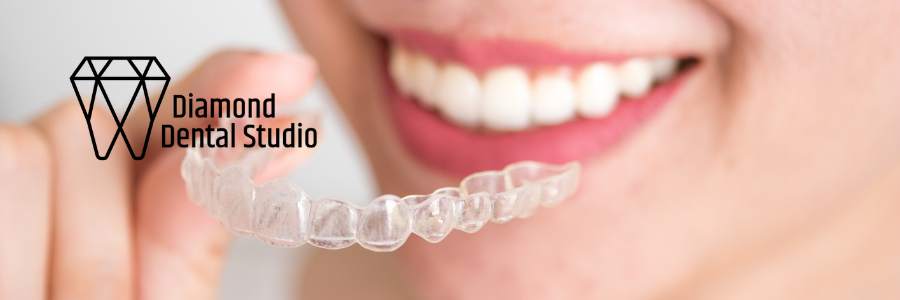 Person holding clear dental aligner near open mouth. Diamond Dental Studio logo on the left.
