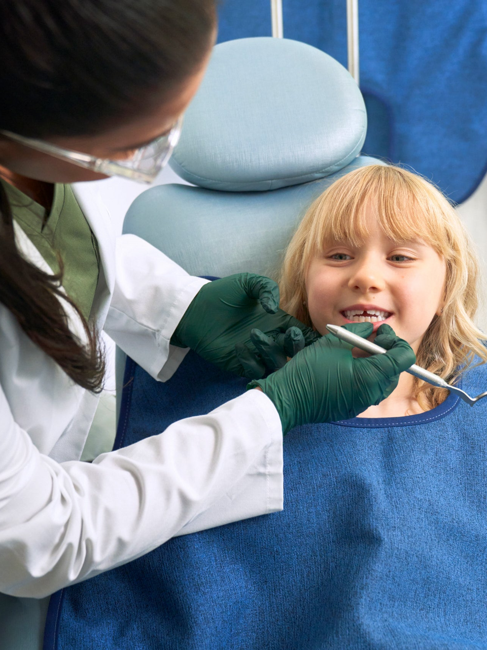 Dentist examining a young blonde child's teeth in a dental chair.