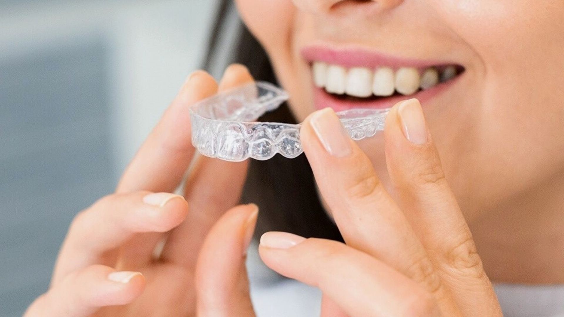Person fitting a clear dental aligner to their teeth, smiling close-up