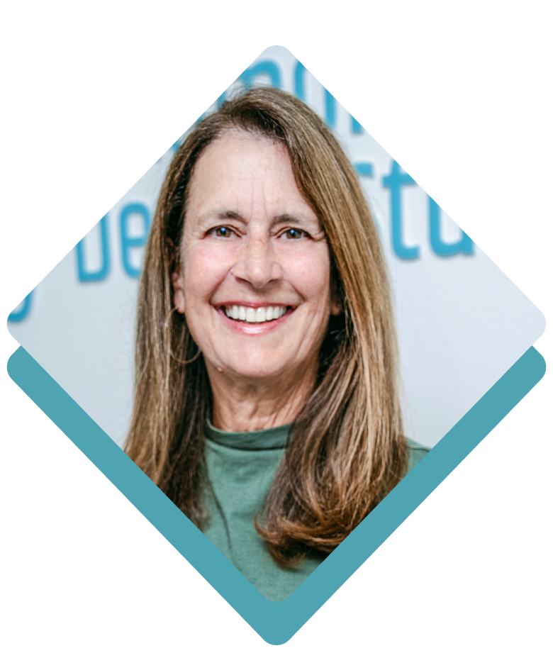 Woman with long brown hair smiles, wearing a green shirt, in front of a turquoise and white background.