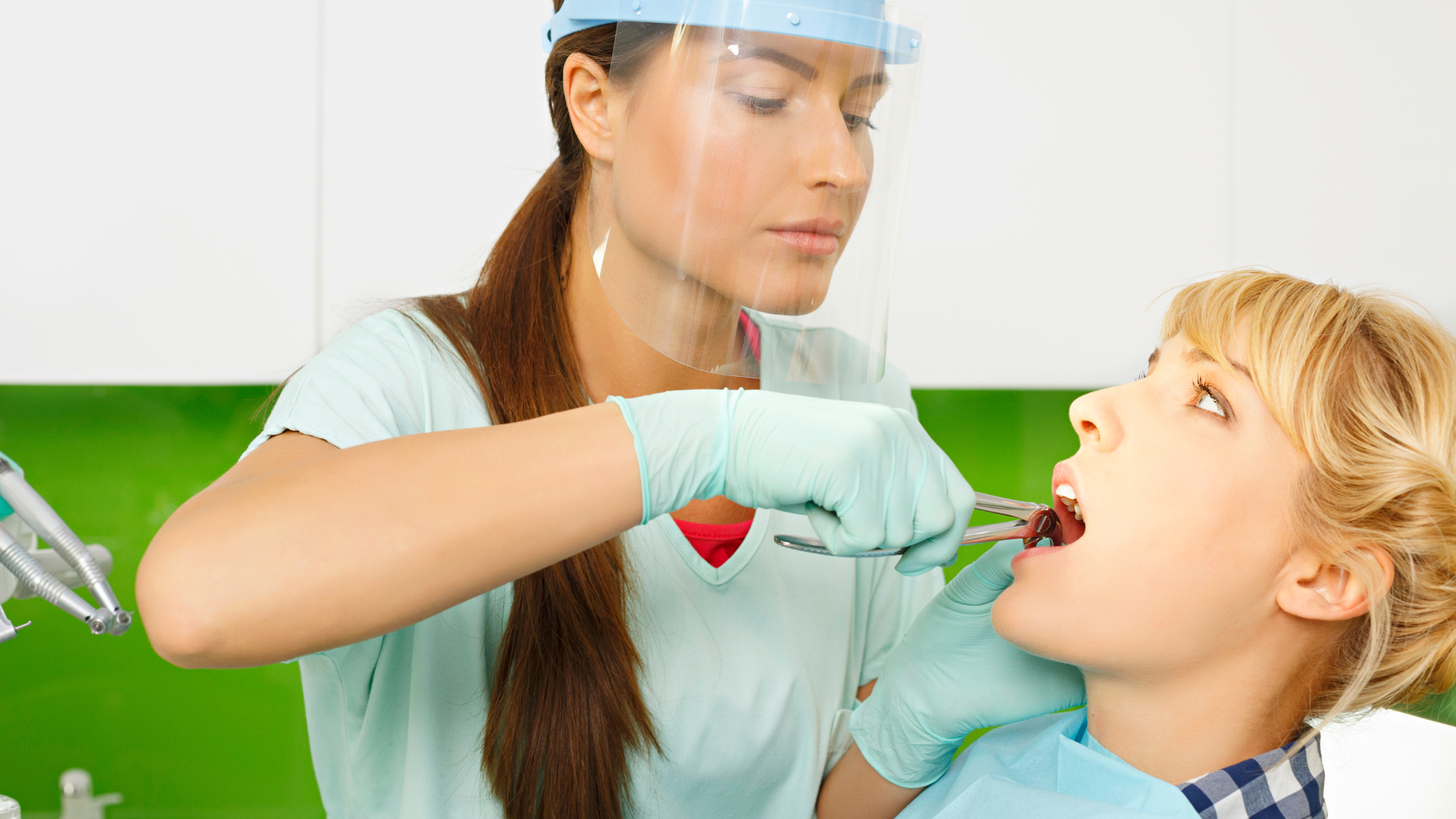 Dentist extracting a tooth from a patient. Both are indoors, the dentist is wearing protective gear.