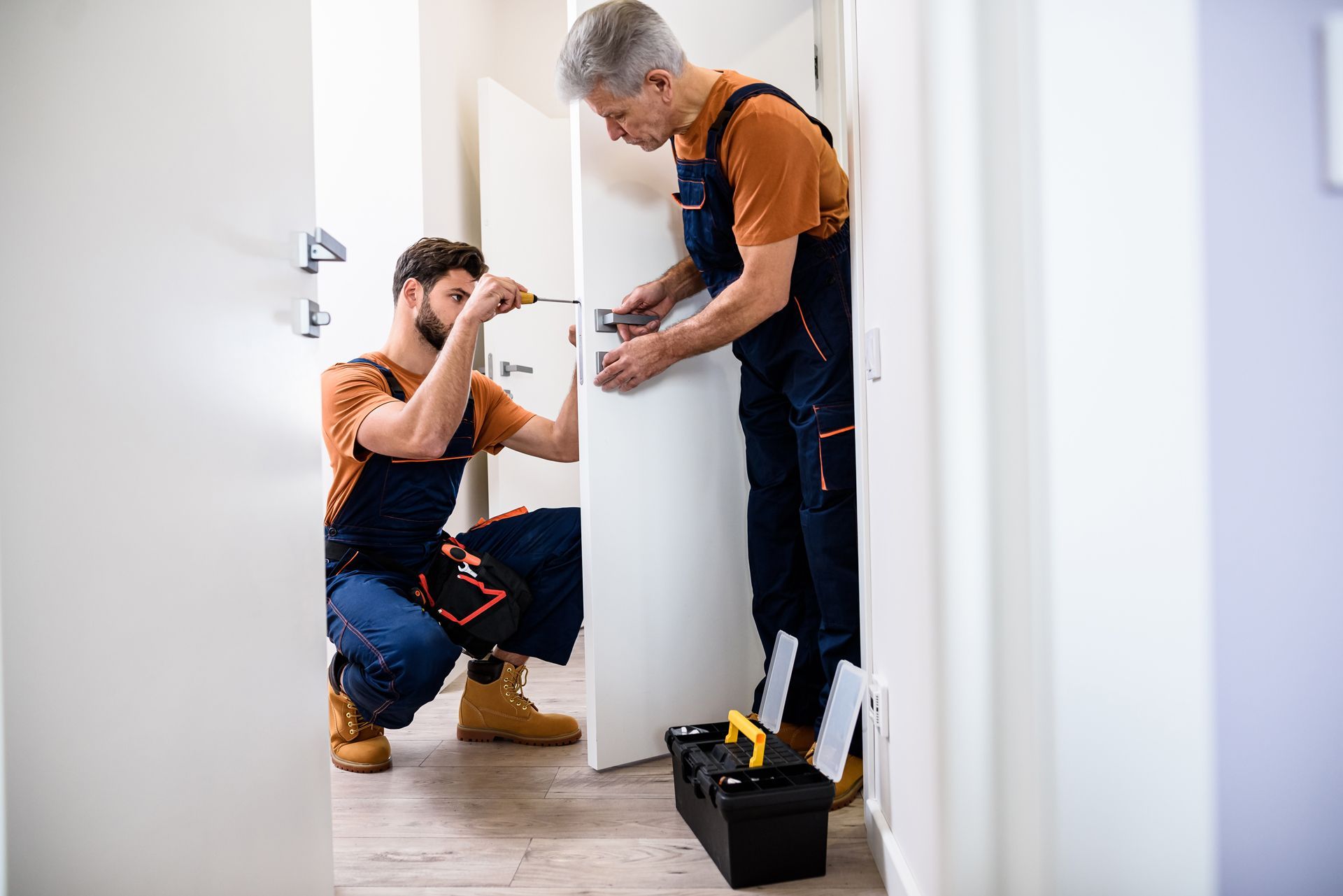 Two people installing a door handle in a doorway.