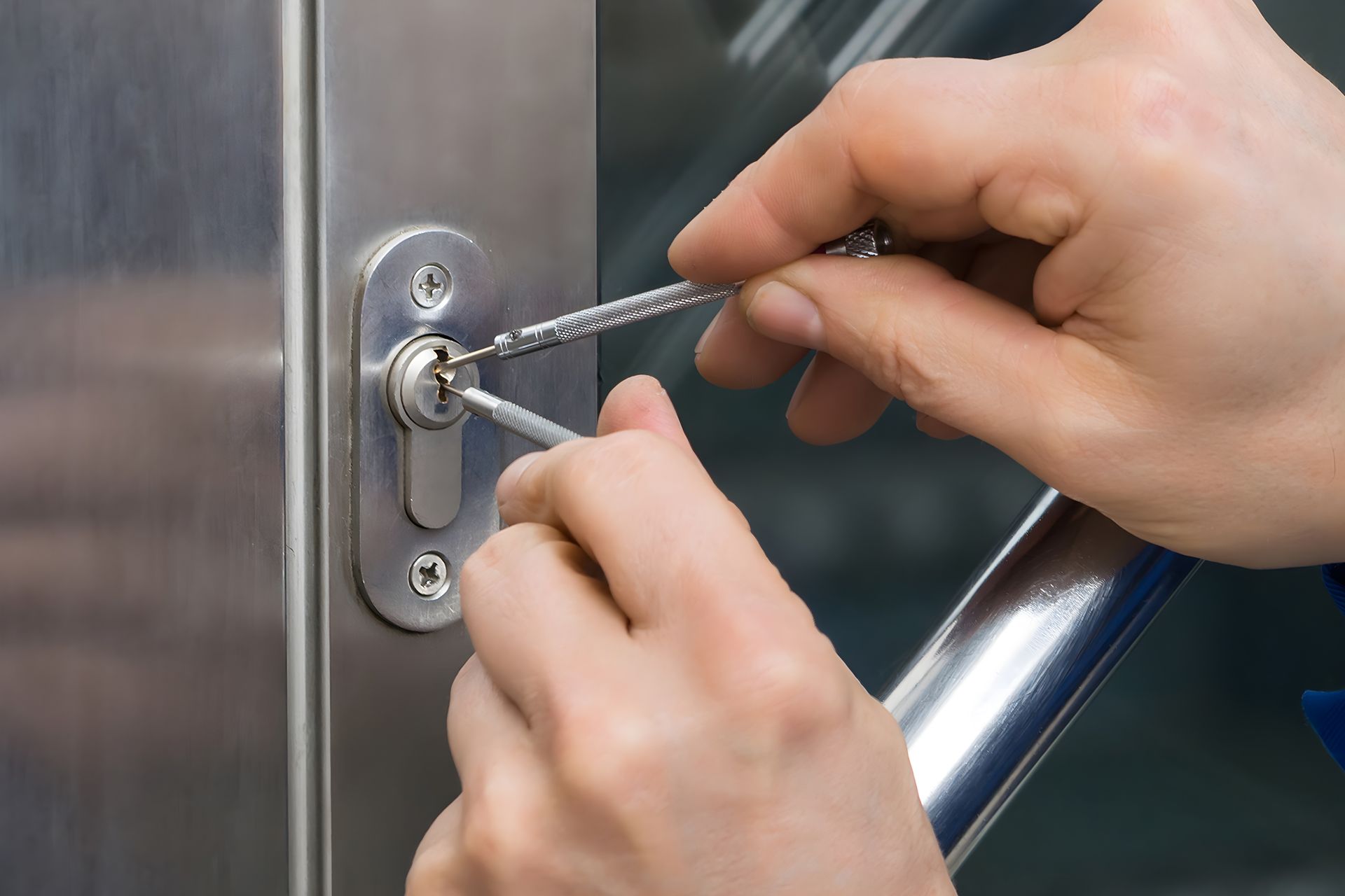 Hands using lock picks to open a metal door lock.