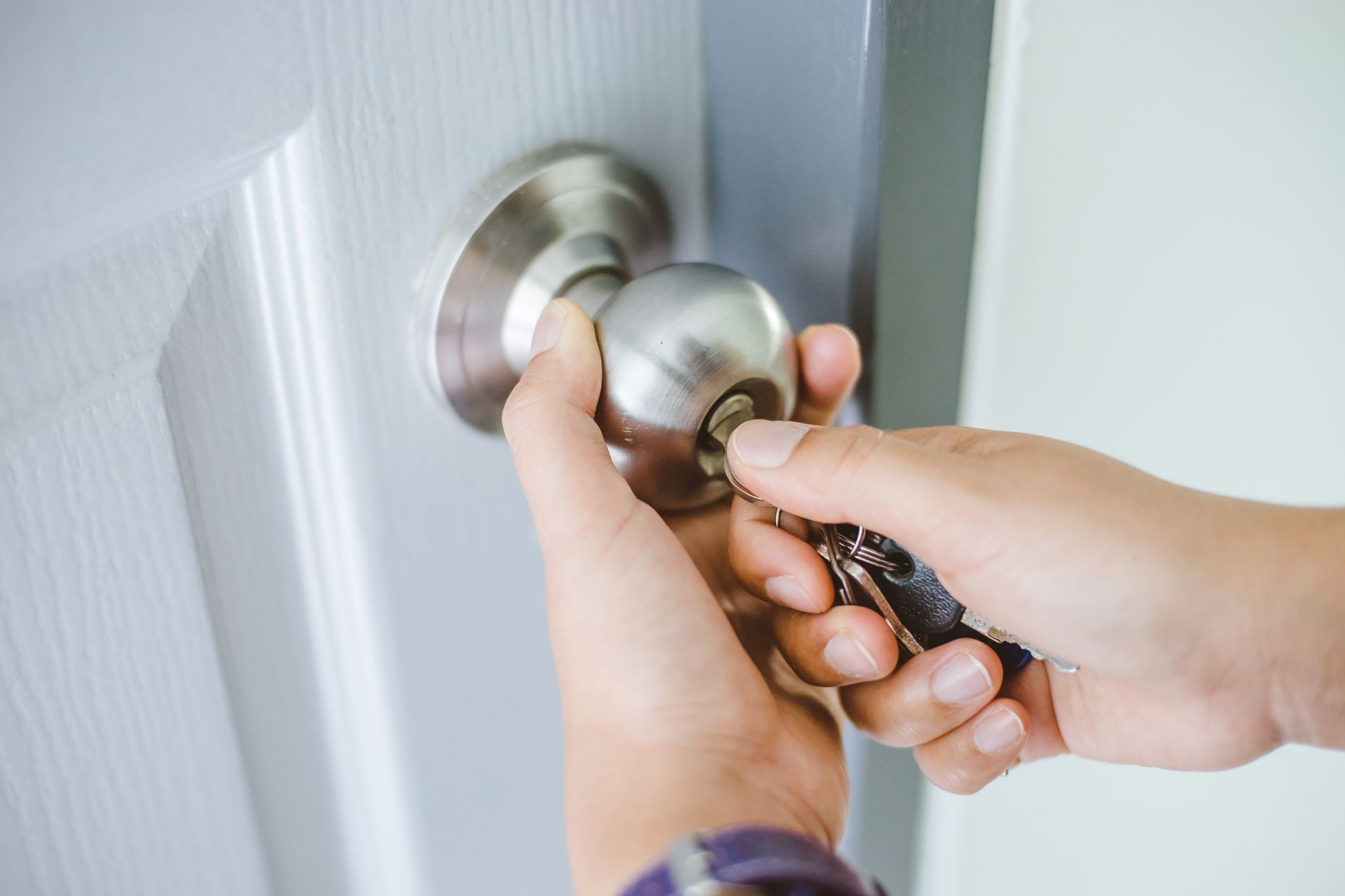 Hands turning a key in a doorknob to unlock a white door.