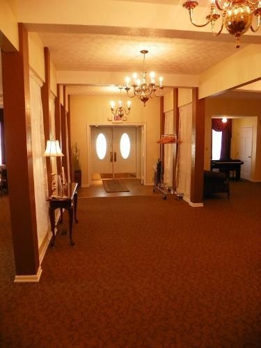 Hallway with brown carpet, two sets of double doors, chandeliers, and decorative pillars.