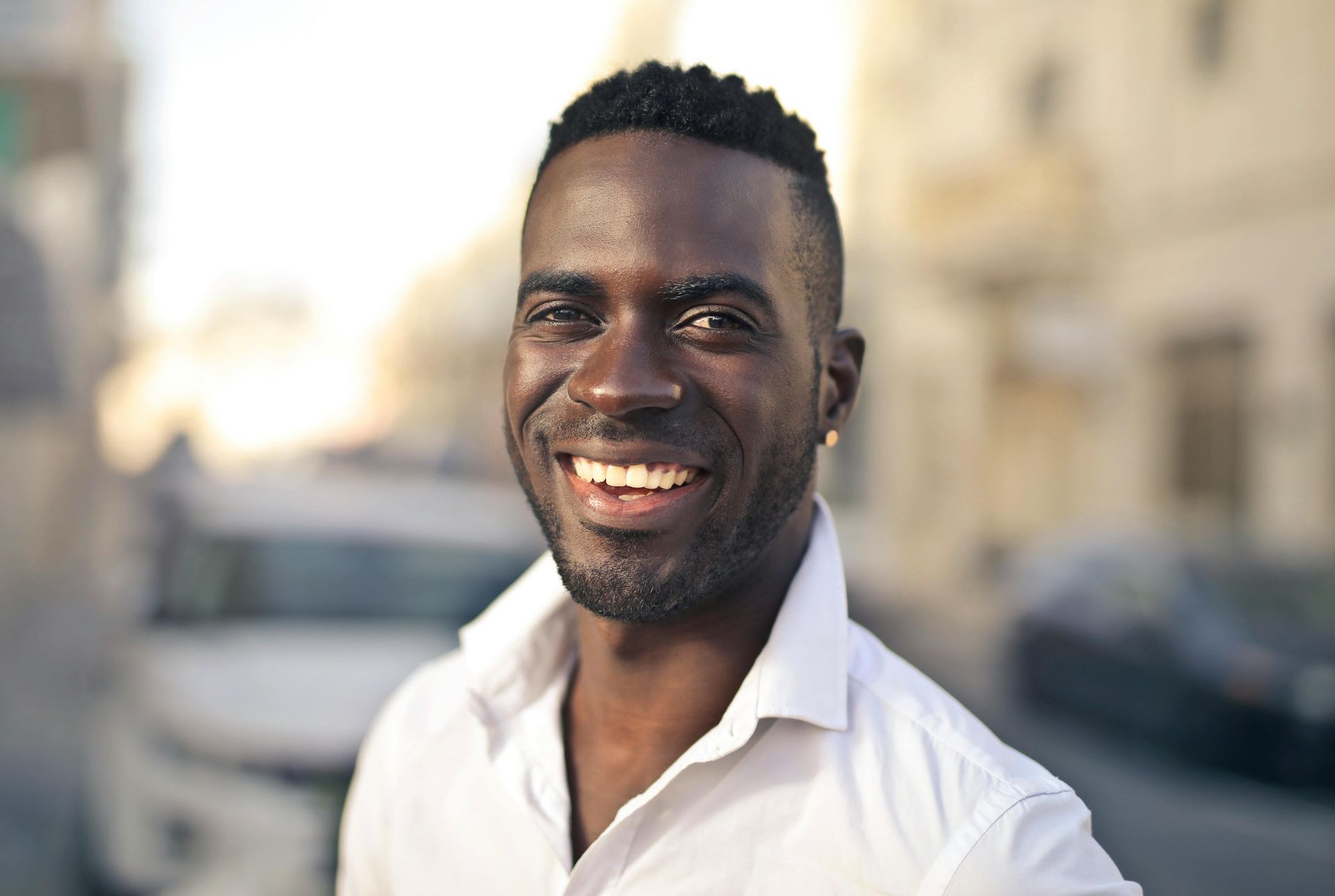 Man in beige sweater smiles while seated on a couch, facing an unseen person.