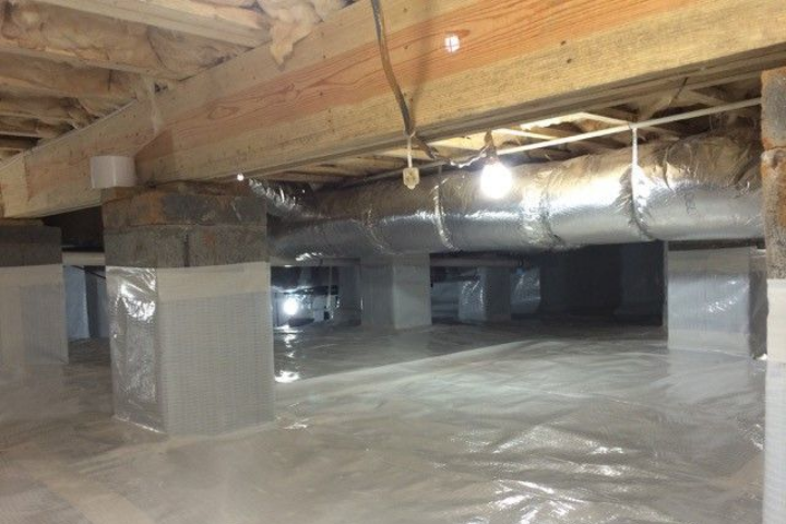 Crawlspace with plastic sheeting, support pillars, ductwork, and insulation under a house.