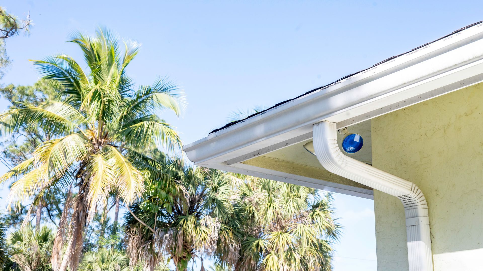 White gutters on a yellow house with a palm tree, clear blue sky.