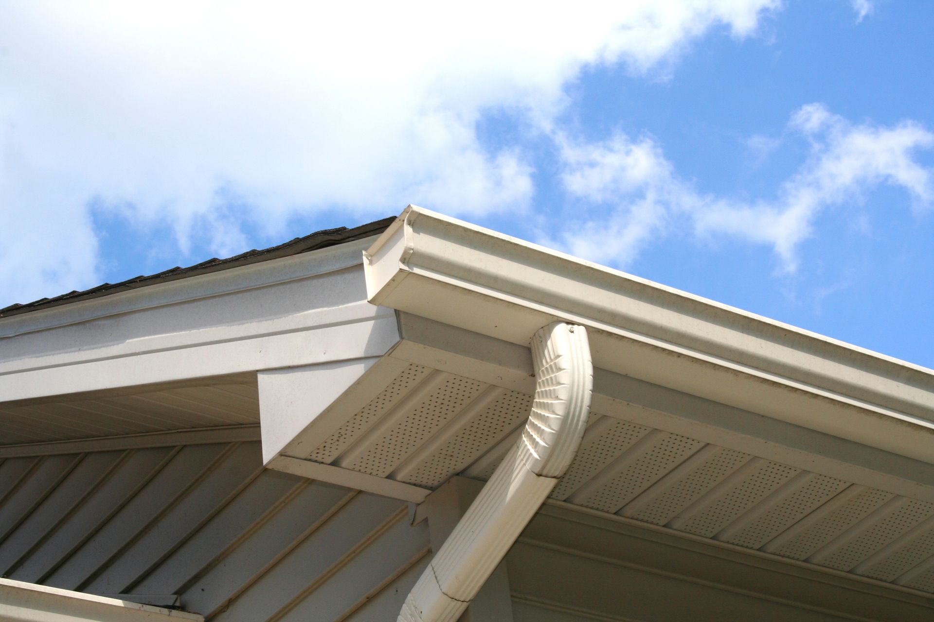 Beige gutters and downspout on a house with a blue sky background.