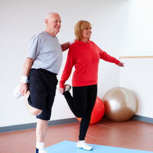 Two people stretching in a bright exercise studio, one in red and one in gray, with stability balls nearby