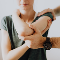 Two hands gently holding an outstretched arm with a dark wristwatch, close-up against a soft background