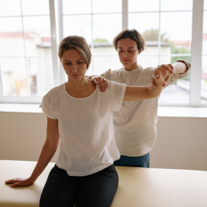 Therapist guiding a seated woman through a shoulder stretch in a bright studio