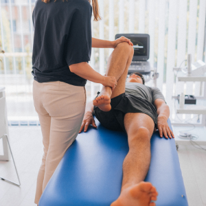 Physical therapist stretching a patient’s leg on a blue treatment table in a bright clinic.