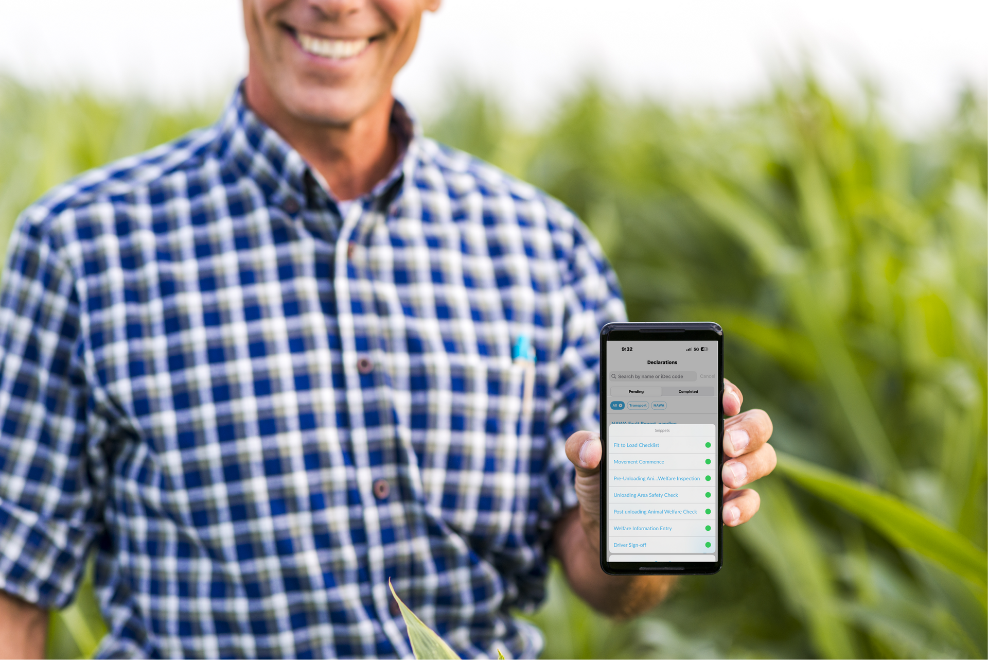 Farmer in plaid shirt smiling, holding phone showing agricultural data in a cornfield.