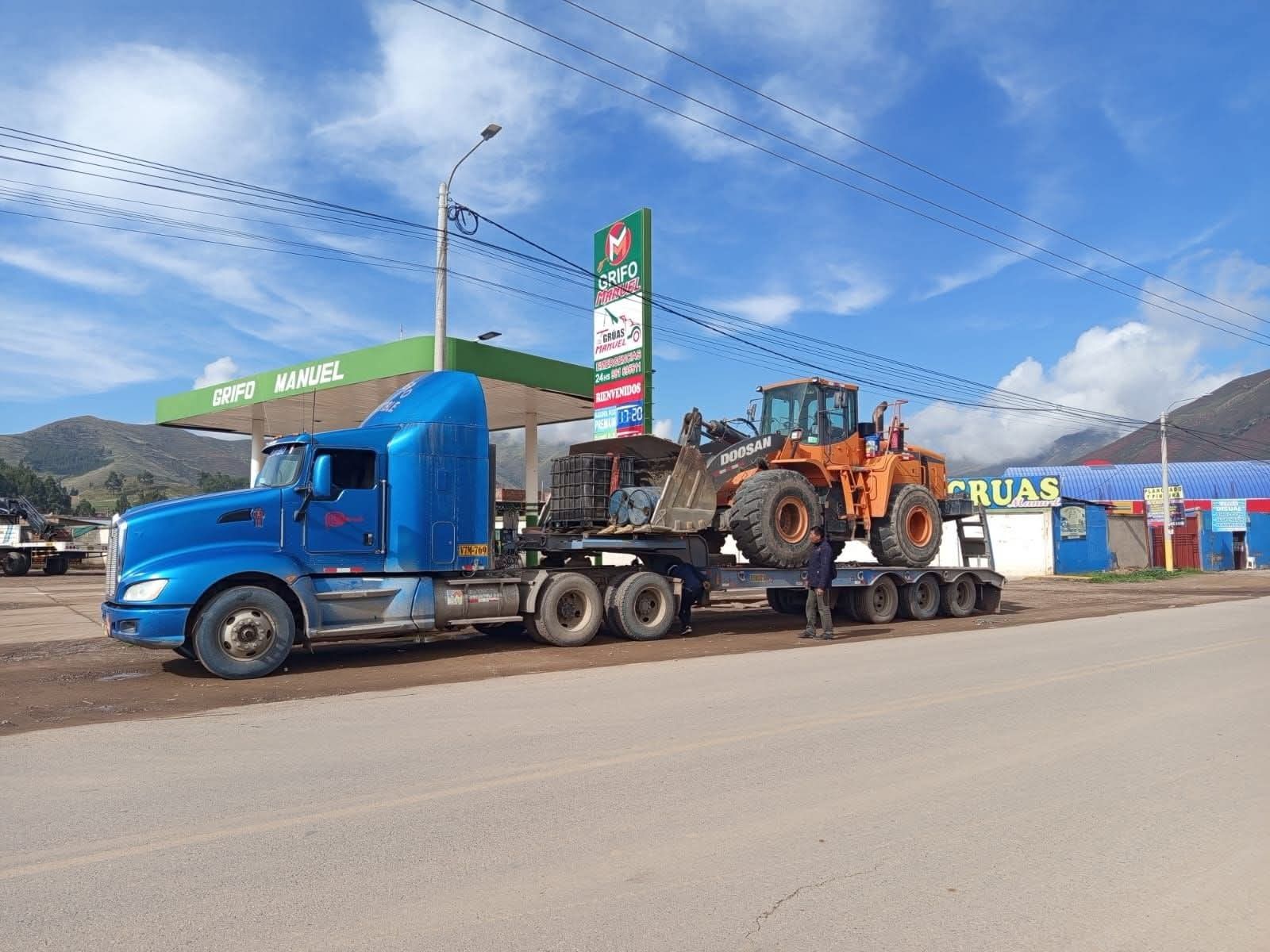Un camión semirremolque azul transporta una excavadora en un remolque.