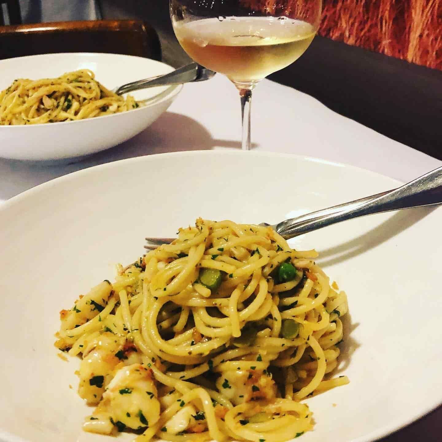 A Plate of Spaghetti With a Fork Next to a Glass of Wine — Onesta Cucina in Bowral, NSW