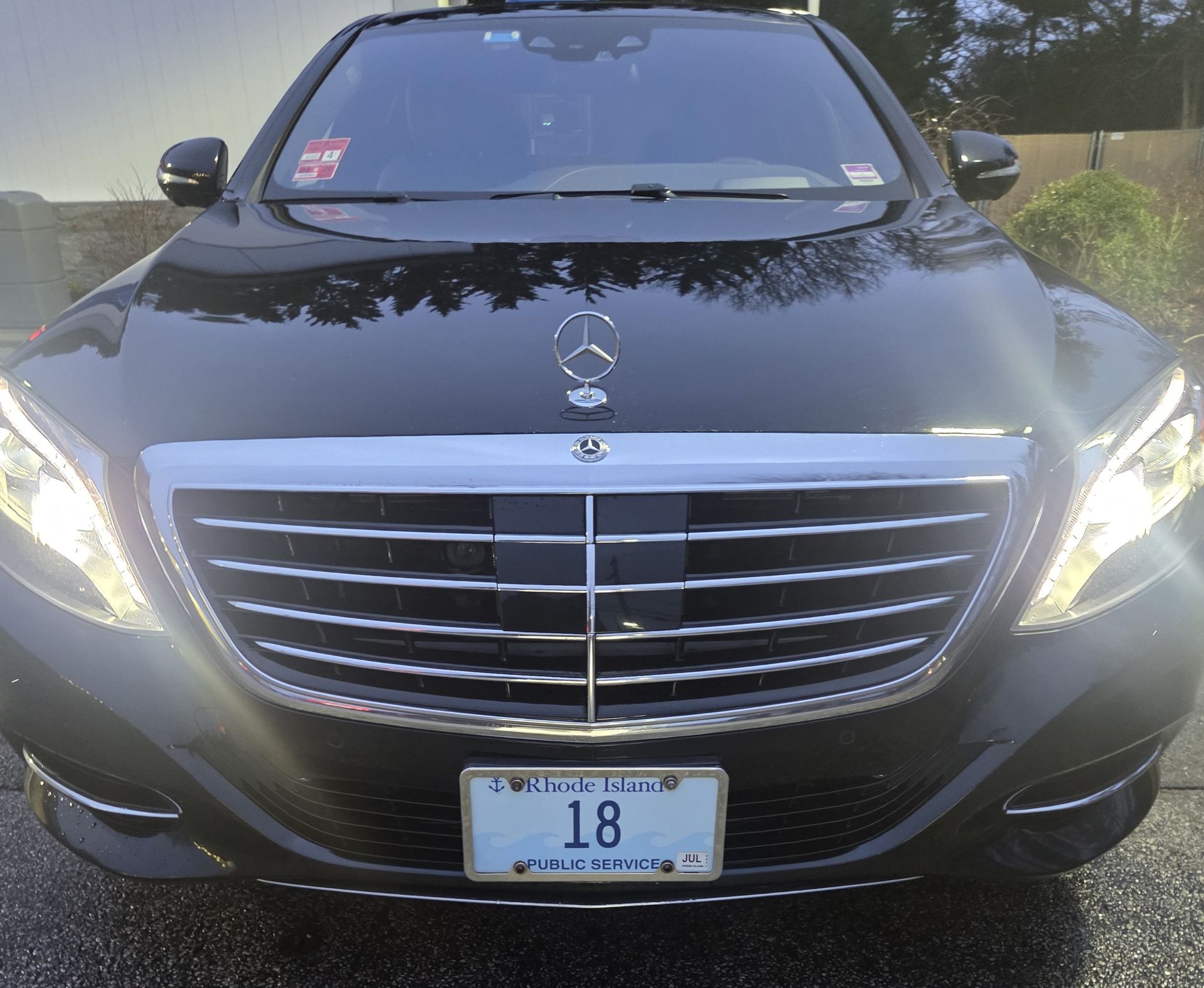 Front view of a black Mercedes sedan with headlights on and license plate 18 in a wet outdoor setting