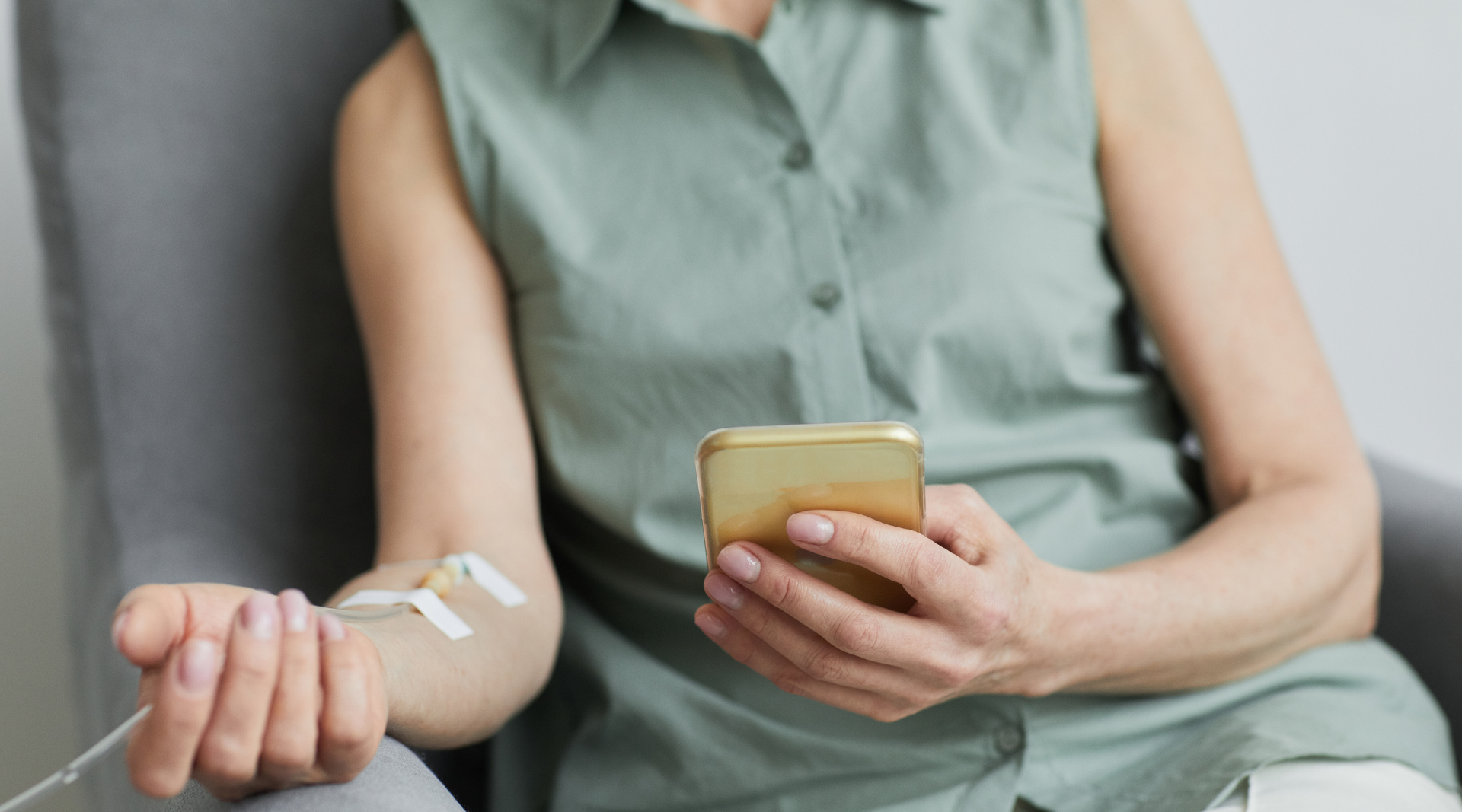 A woman is sitting in a chair with an iv in her arm and using a cell phone while performing
