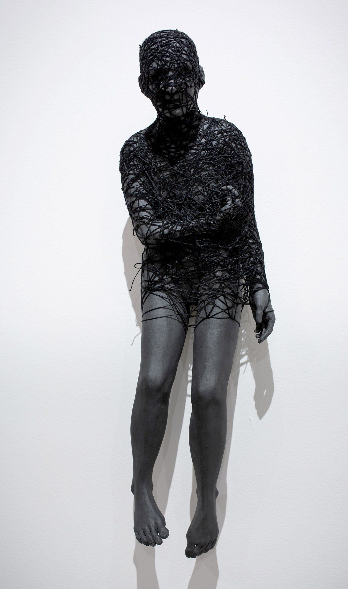 A black statue of a person sitting on a wall.