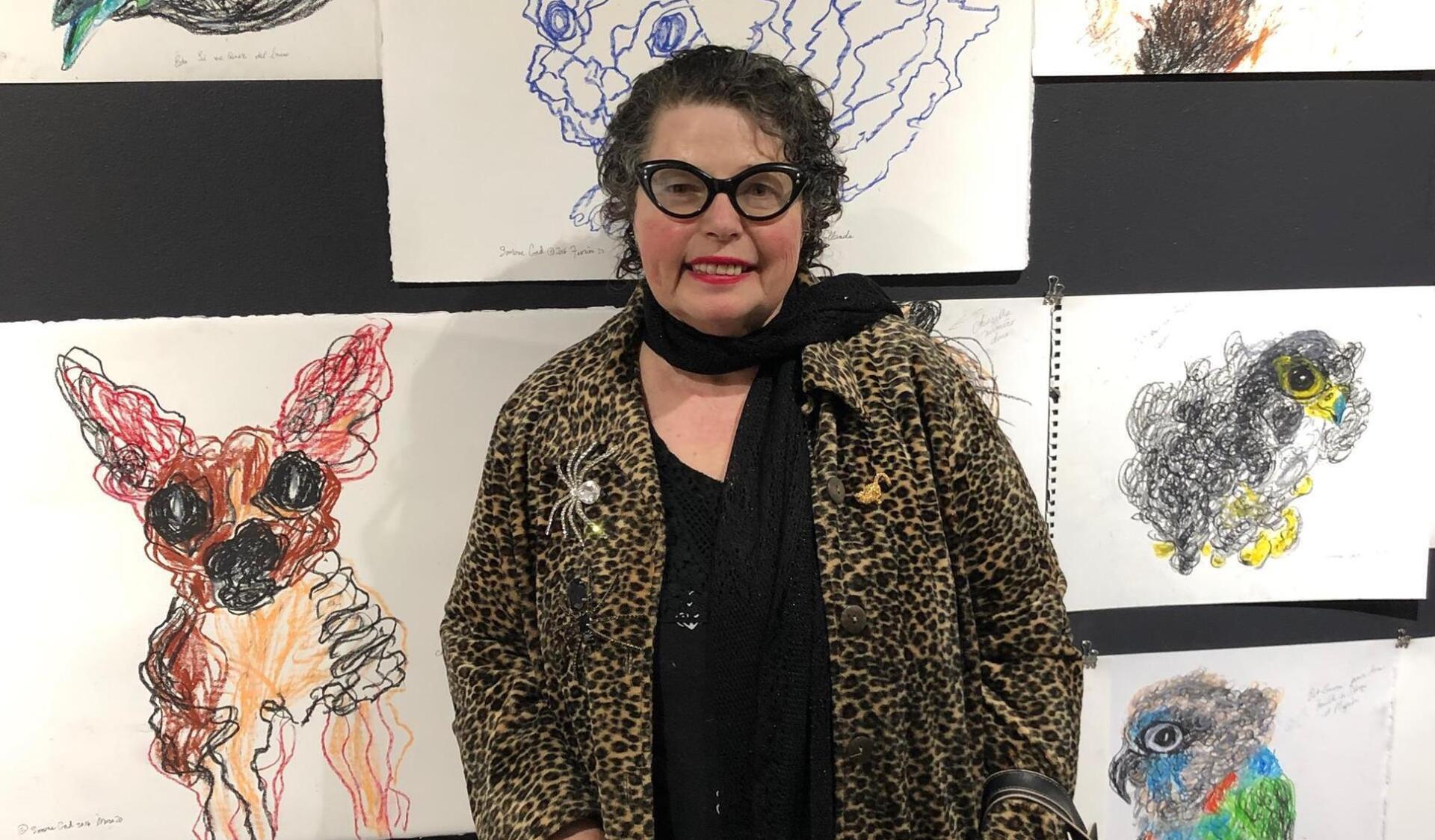 A woman in a leopard print jacket is standing in front of a wall of paintings.