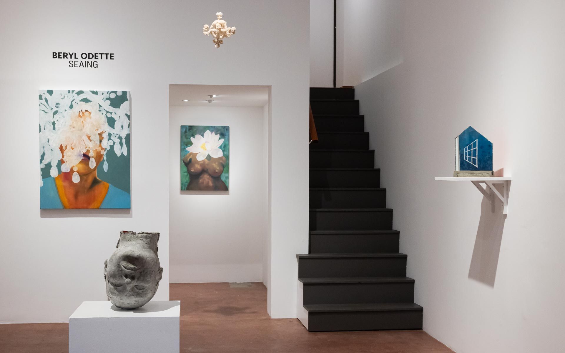 Large blue painting of flowers under water, a small orange portrait and a ceramic vessel on a pedestal beside a glass storefront. Installation view, Beryl Odette: Seaing, Track 16.