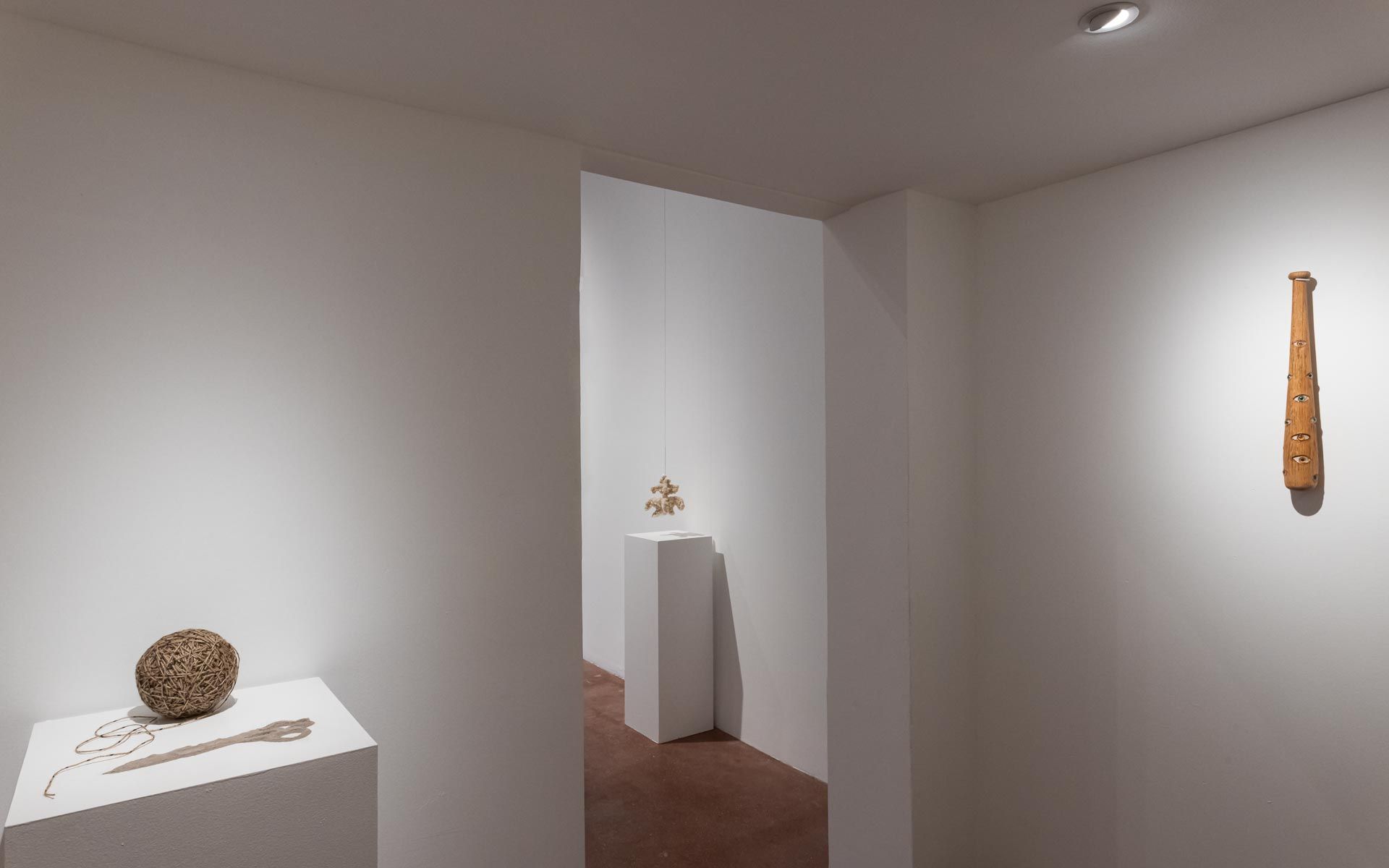 Woven spherical ceramic on a white pedestal, a small gold sculpture on a tall pedestal and a wooden club-shaped piece on the right wall. Installation view, Beryl Odette: Seaing, Track 16.