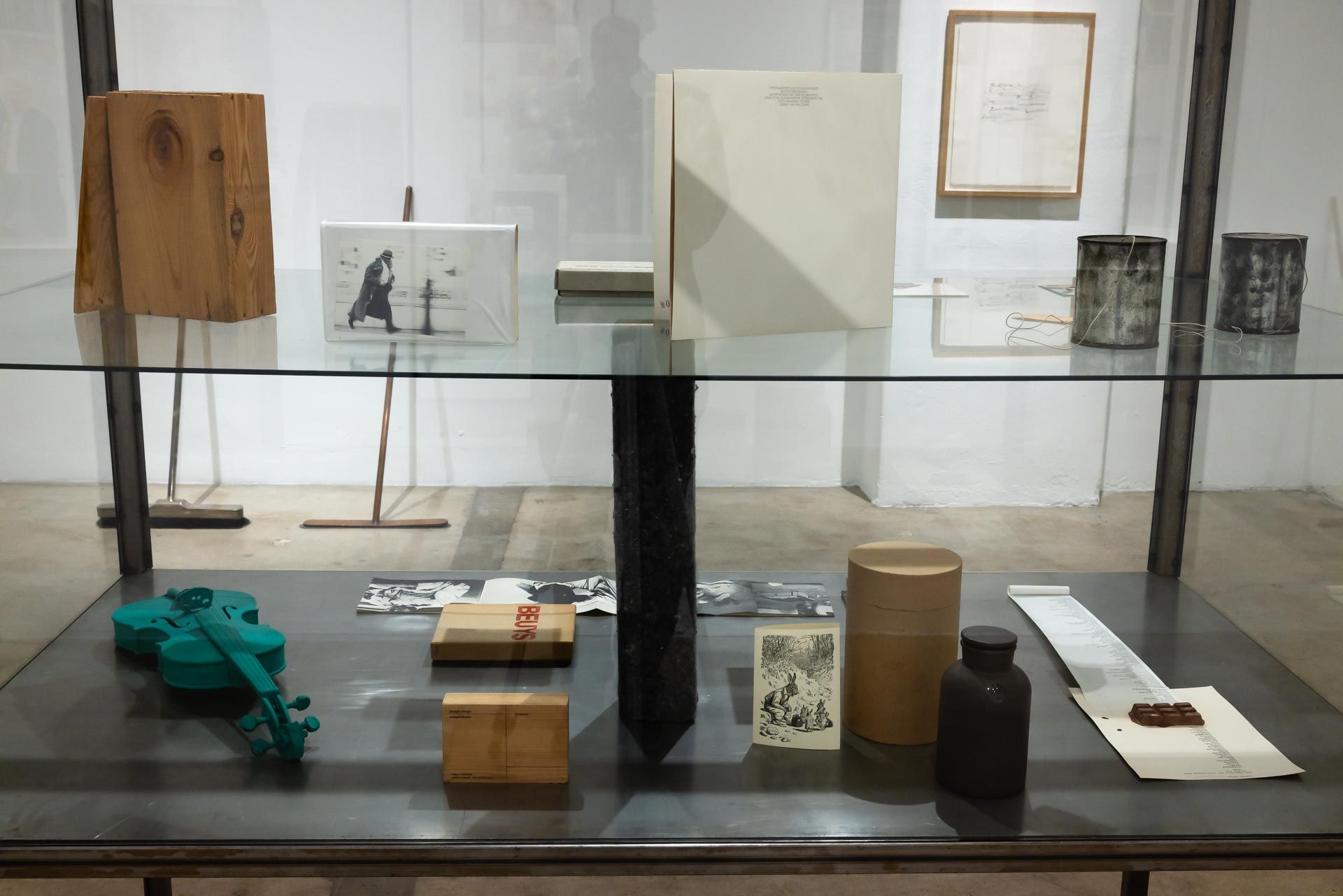 Museum display of small mixed-media artworks arranged on glass shelves in a minimalist room. TRACK 16 | DOWNTOWN LA art exhibition and retrospective of JOSEPH BEUYS titled POTENTIAL GOODS. Sculpture, mixed media and drawings.