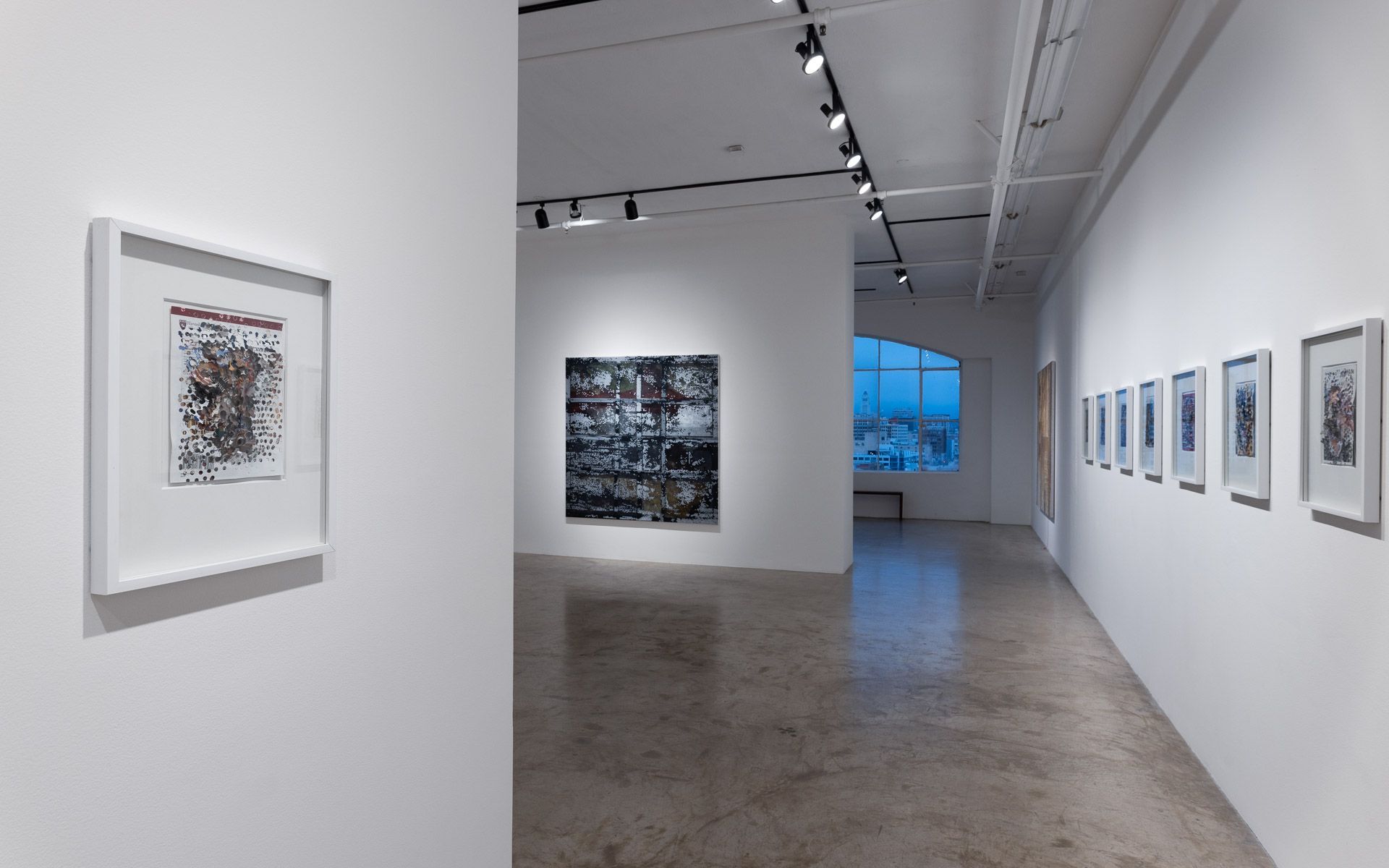 Framed work in a white frame at left, a dark perforated panel beyond, and a row of small framed works along the right wall. Installation view, David Daigle: Trypophobic Panopticons, Track 16.