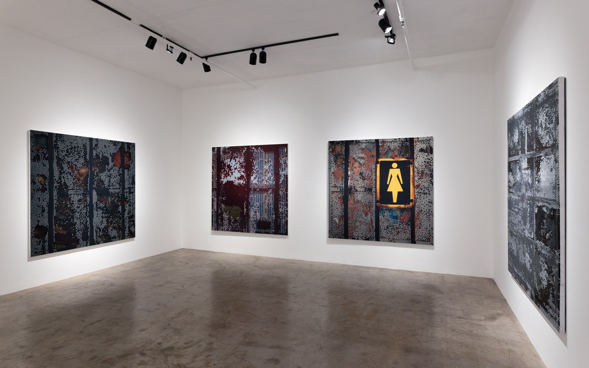 Dark perforated panels along two white walls, with a yellow woman pictogram on the center panel and a tall panel at right. Installation view, David Daigle: Trypophobic Panopticons, Track 16.