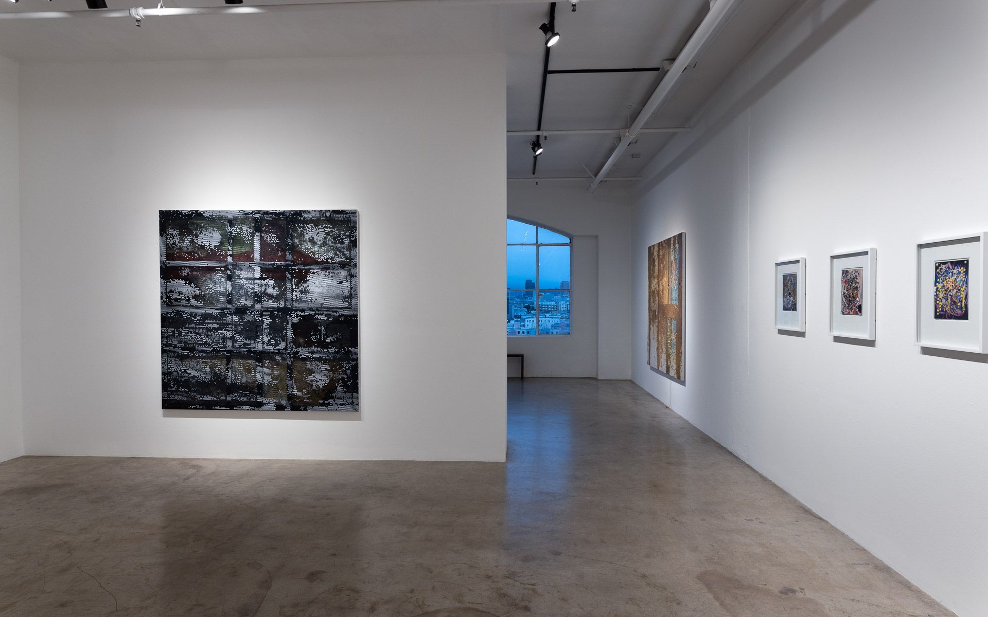 Dark blue-black perforated panel on the back wall and a maroon-toned panel on the right wall, with a third panel down the hall at left. Installation view, David Daigle: Trypophobic Panopticons, Track 16.