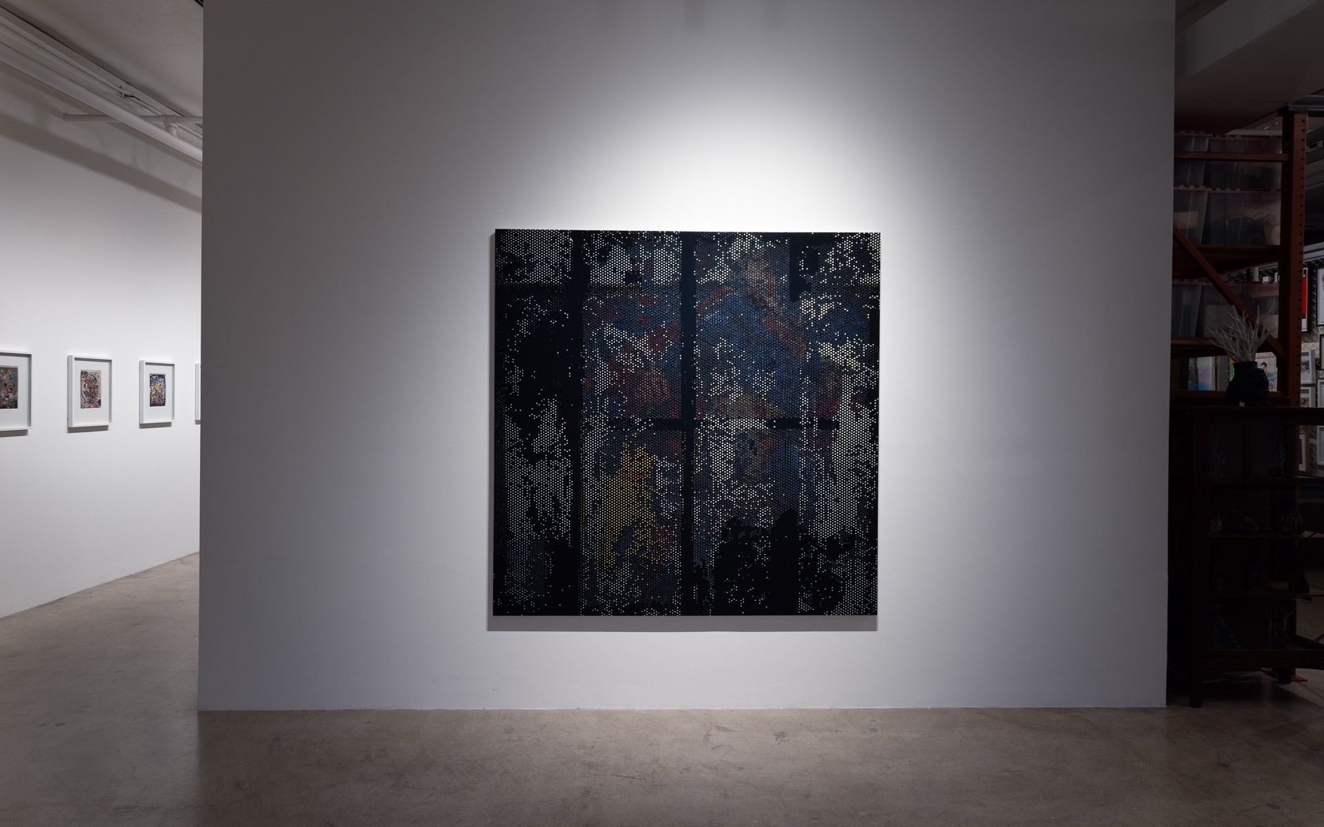 Large dark perforated panel centered on a white wall, with small framed works on the wall at left. Installation view, David Daigle: Trypophobic Panopticons, Track 16.
