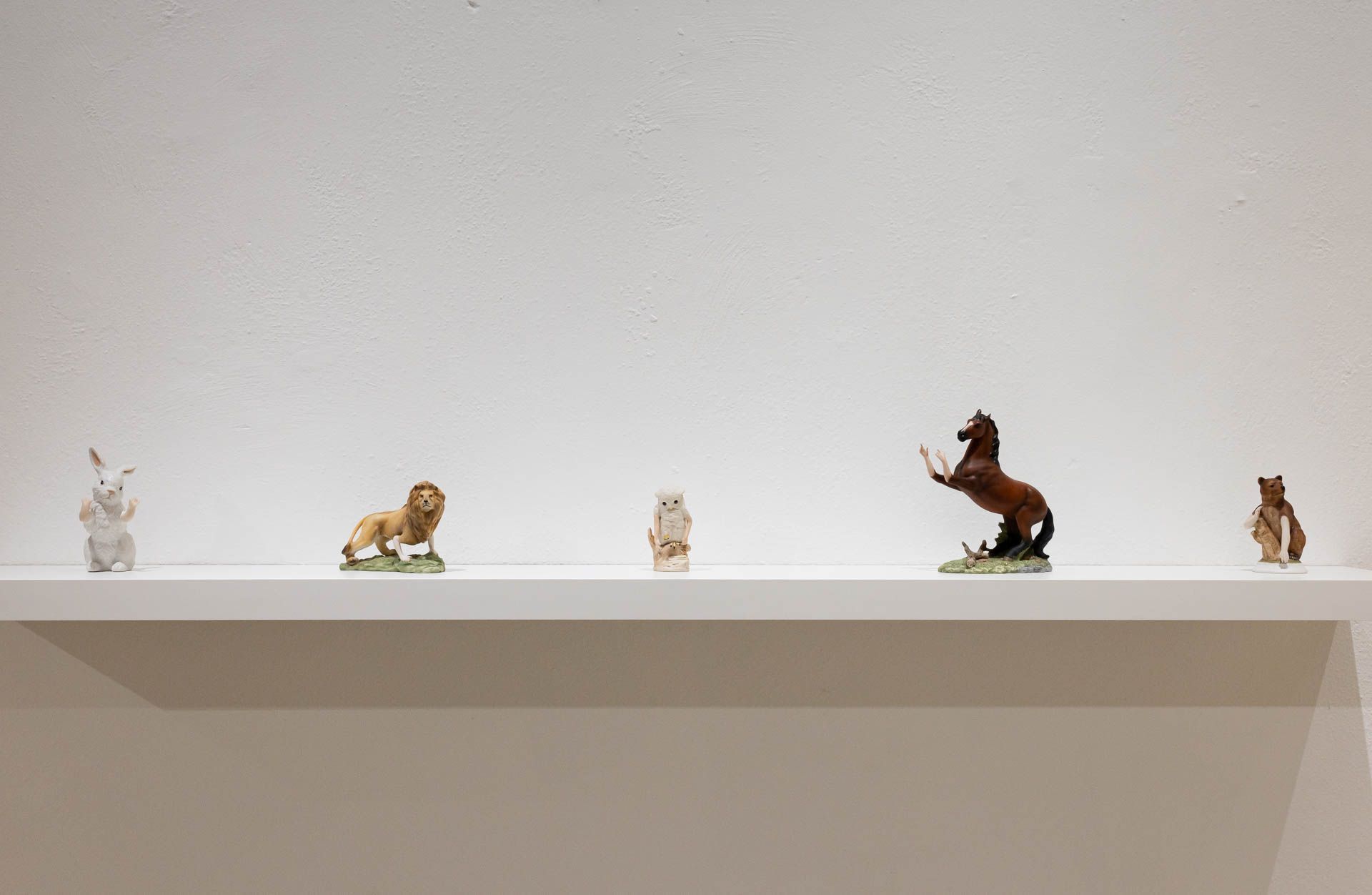 White wall shelf with small ceramic animals: a white rabbit, a lion, a horse rearing on its hind legs and a bear. Installation view, Debra Broz: Strange World, Track 16.