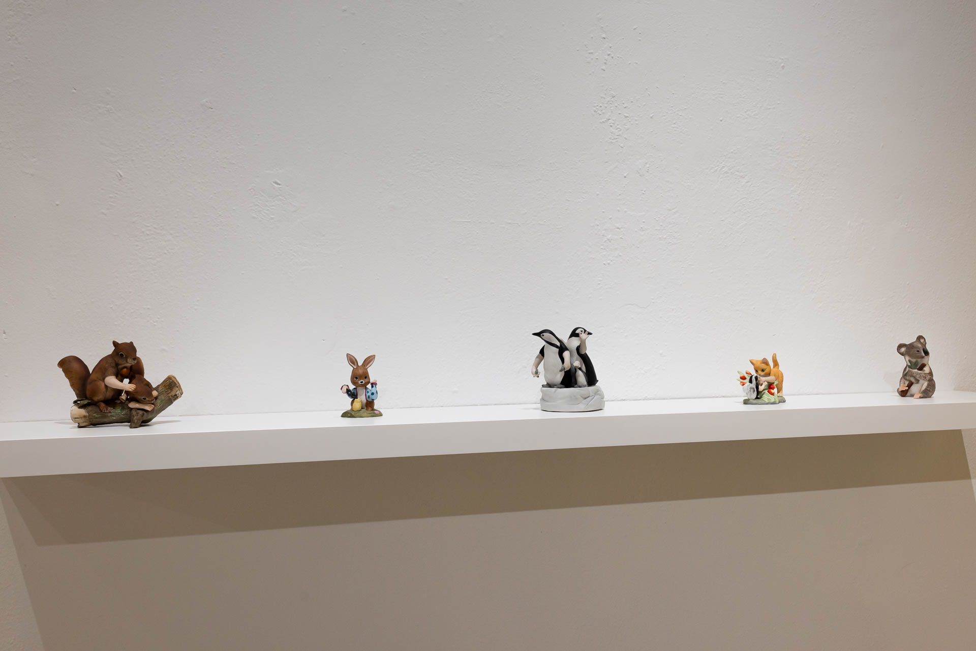 White wall shelf with small figurines: a squirrel, a rabbit, penguins, a fox and a koala. Installation view, Debra Broz: Strange World, Track 16.