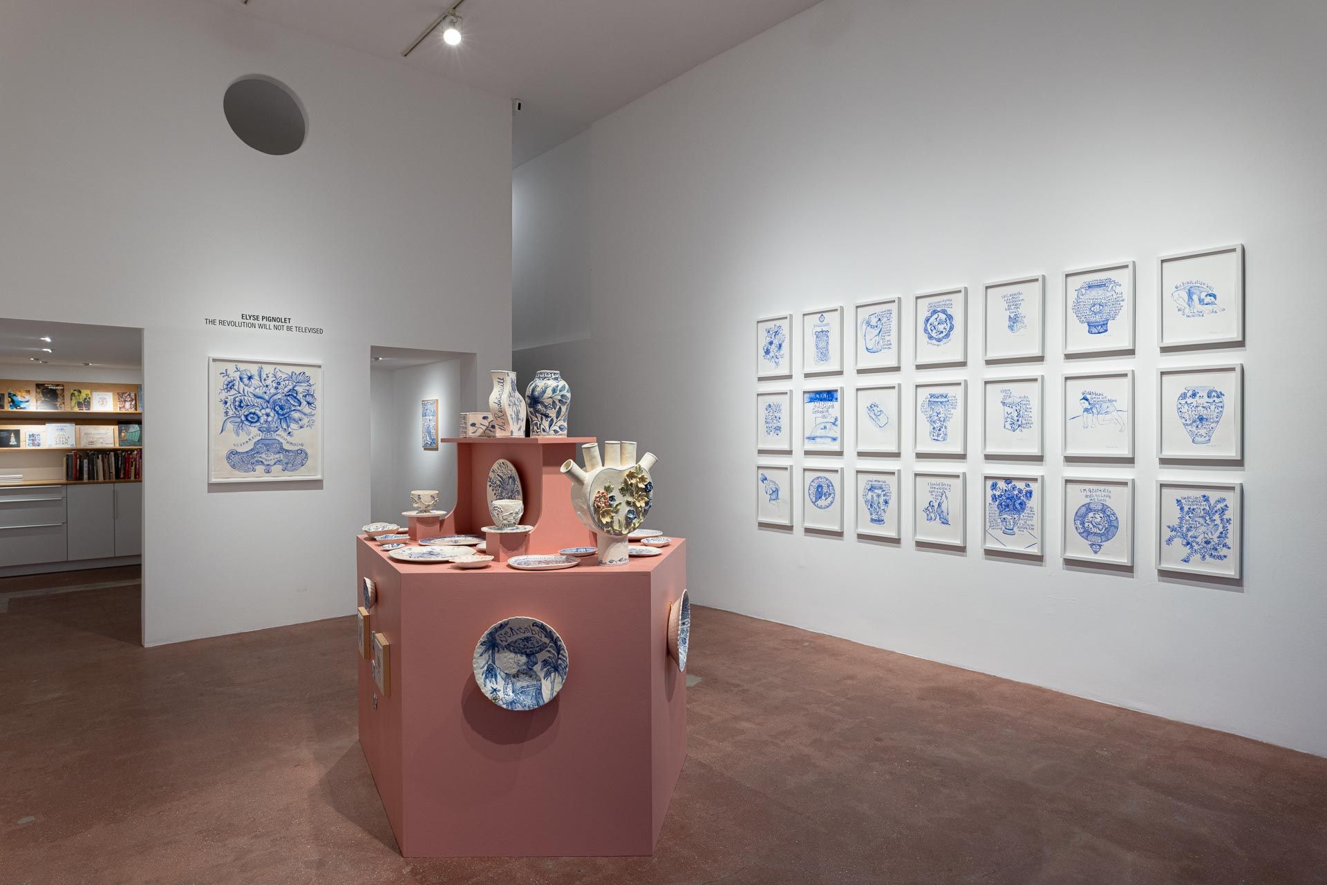 Art gallery room with pink pedestals displaying blue-and-white ceramics and framed blue artworks on white walls. Elyse Pignolet art exhibition at Track 16 East Hollywood gallery. Title, The Revolution Will Not Be Televised featuring ceramic works and drawings.