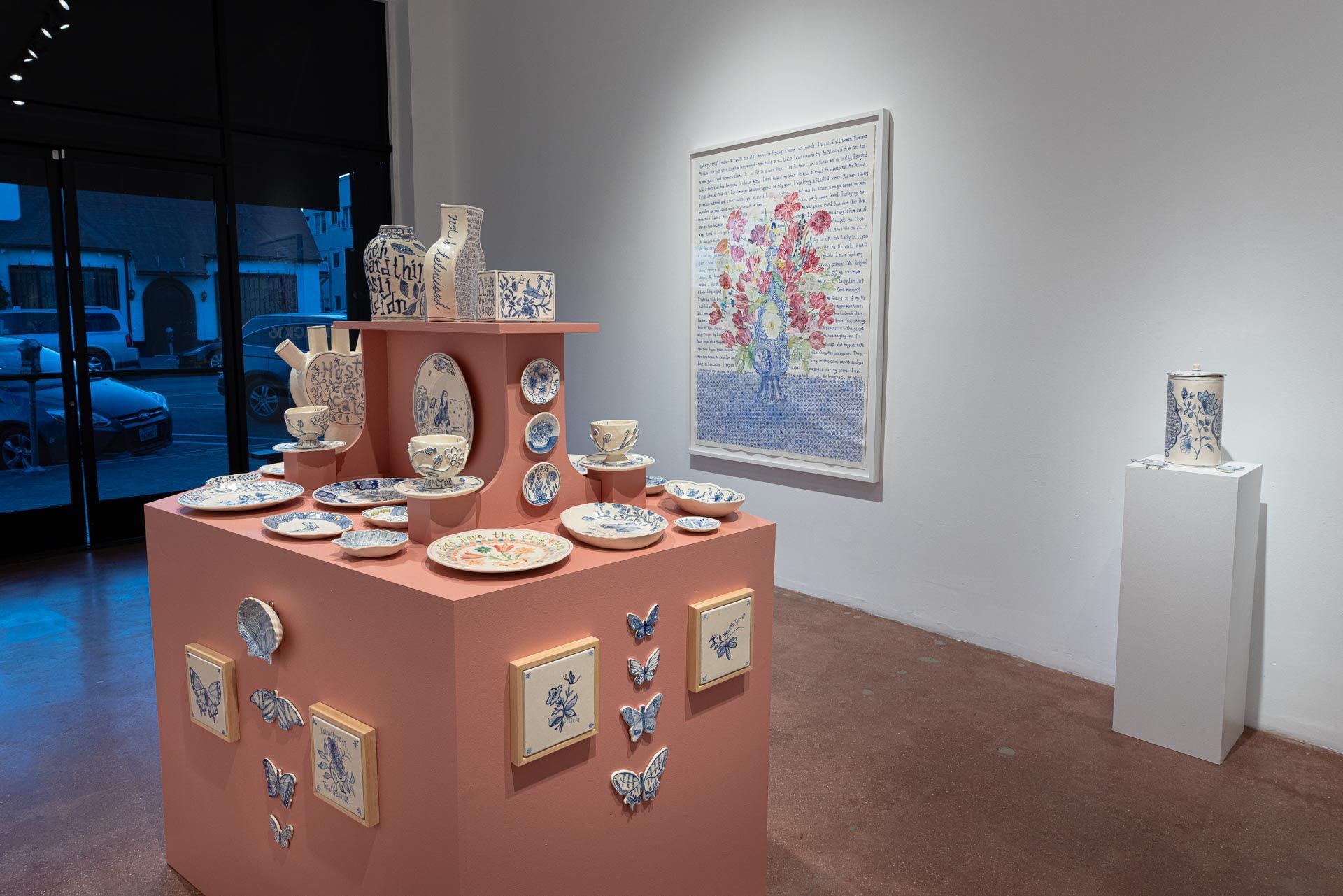 Ceramic art display in a gallery with pink pedestal, wall art, and a small sculpture on a white pedestal. Elyse Pignolet art exhibition at Track 16 East Hollywood gallery. Title, The Revolution Will Not Be Televised featuring ceramic works and drawings.