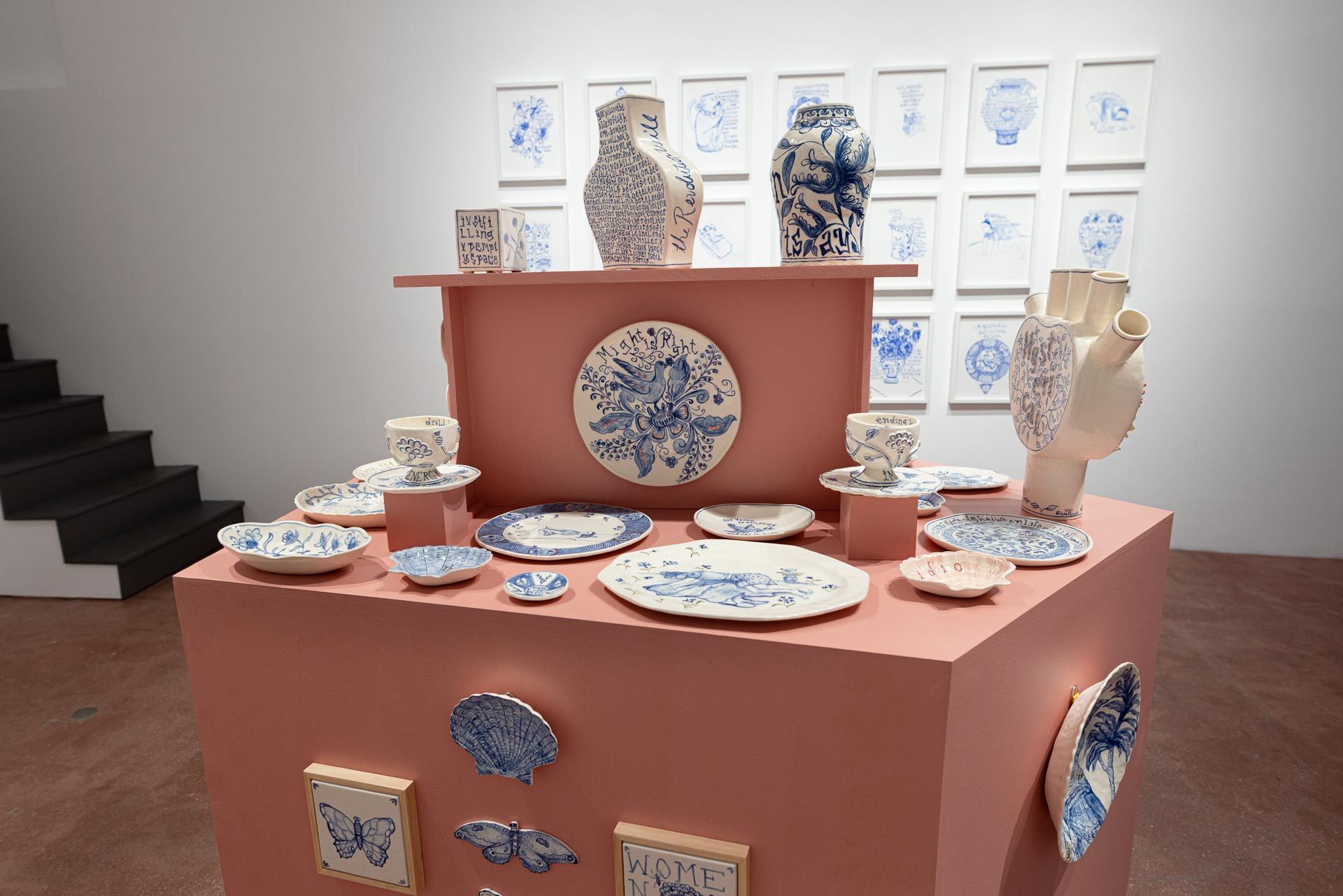 Ceramic dish display on pink pedestals in a gallery, with blue-and-white plates and vases. Elyse Pignolet art exhibition at Track 16 East Hollywood gallery. Title, The Revolution Will Not Be Televised featuring ceramic works and drawings.