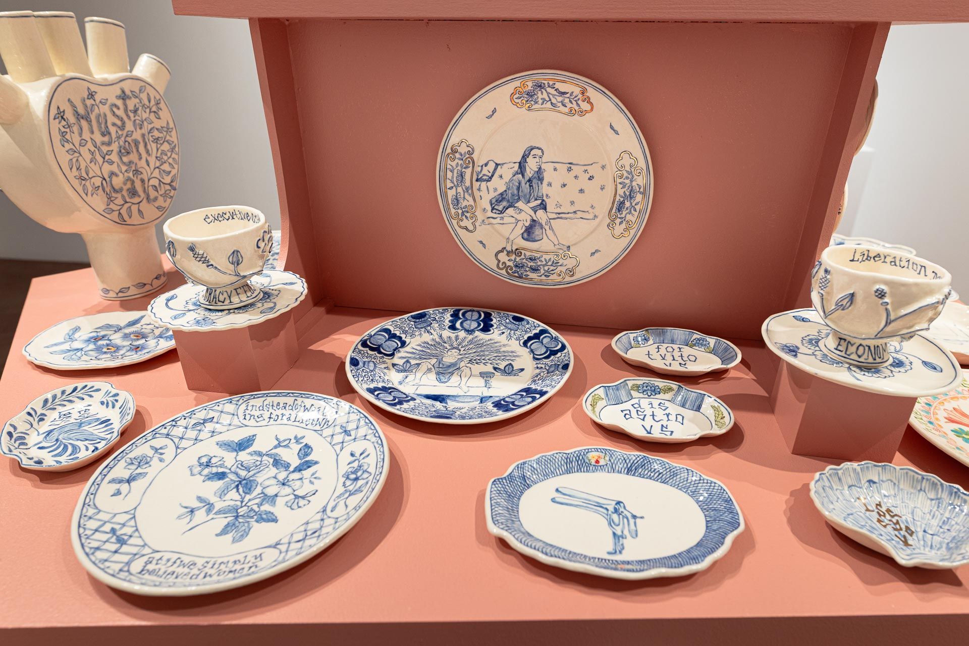 Blue-and-white floral plates and ceramics displayed on a terracotta shelf and backdrop. Elyse Pignolet art exhibition at Track 16 East Hollywood gallery. Title, The Revolution Will Not Be Televised featuring ceramic works and drawings.