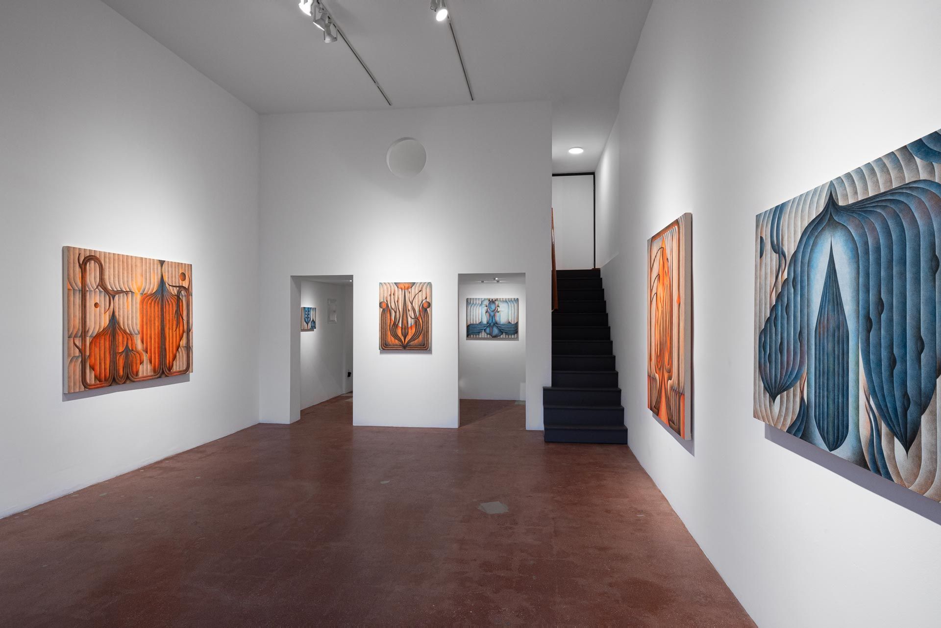 Gallery view with orange paintings at left, a large blue painting at right, a dark staircase. Installation view, Roberta Gentry: Blood Orange, Track 16, Los Angeles.
