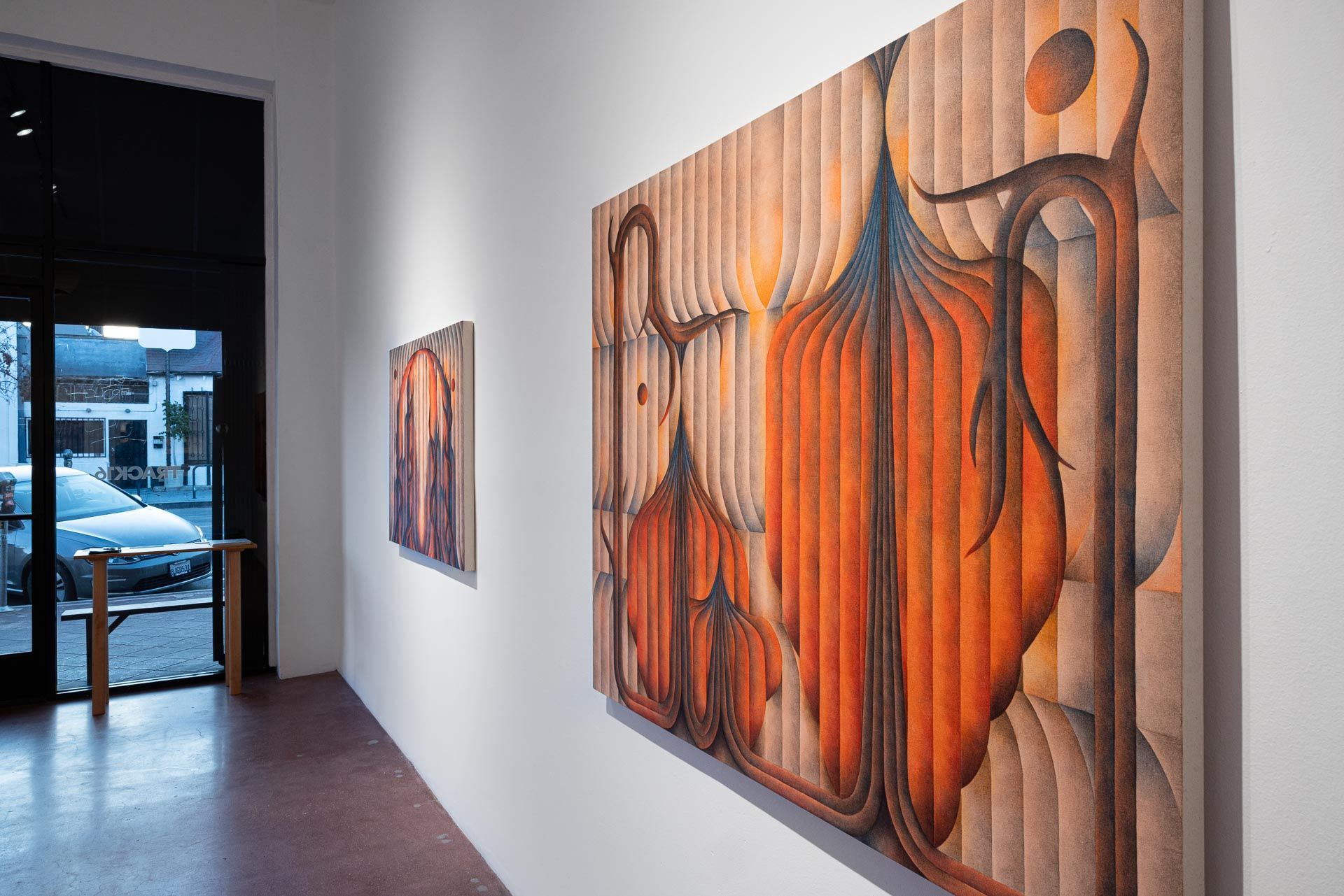 Large orange painting seen at an angle, a second beyond it, glass door at left. Installation view, Roberta Gentry: Blood Orange, Track 16, Los Angeles.