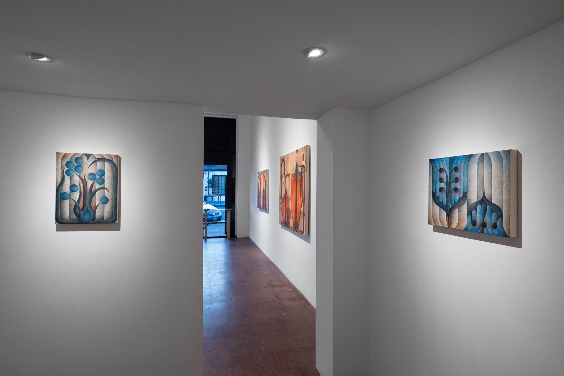Dusk view through the storefront window, orange paintings inside, blue title lettering on the glass. Installation view, Roberta Gentry: Blood Orange, Track 16, Los Angeles.