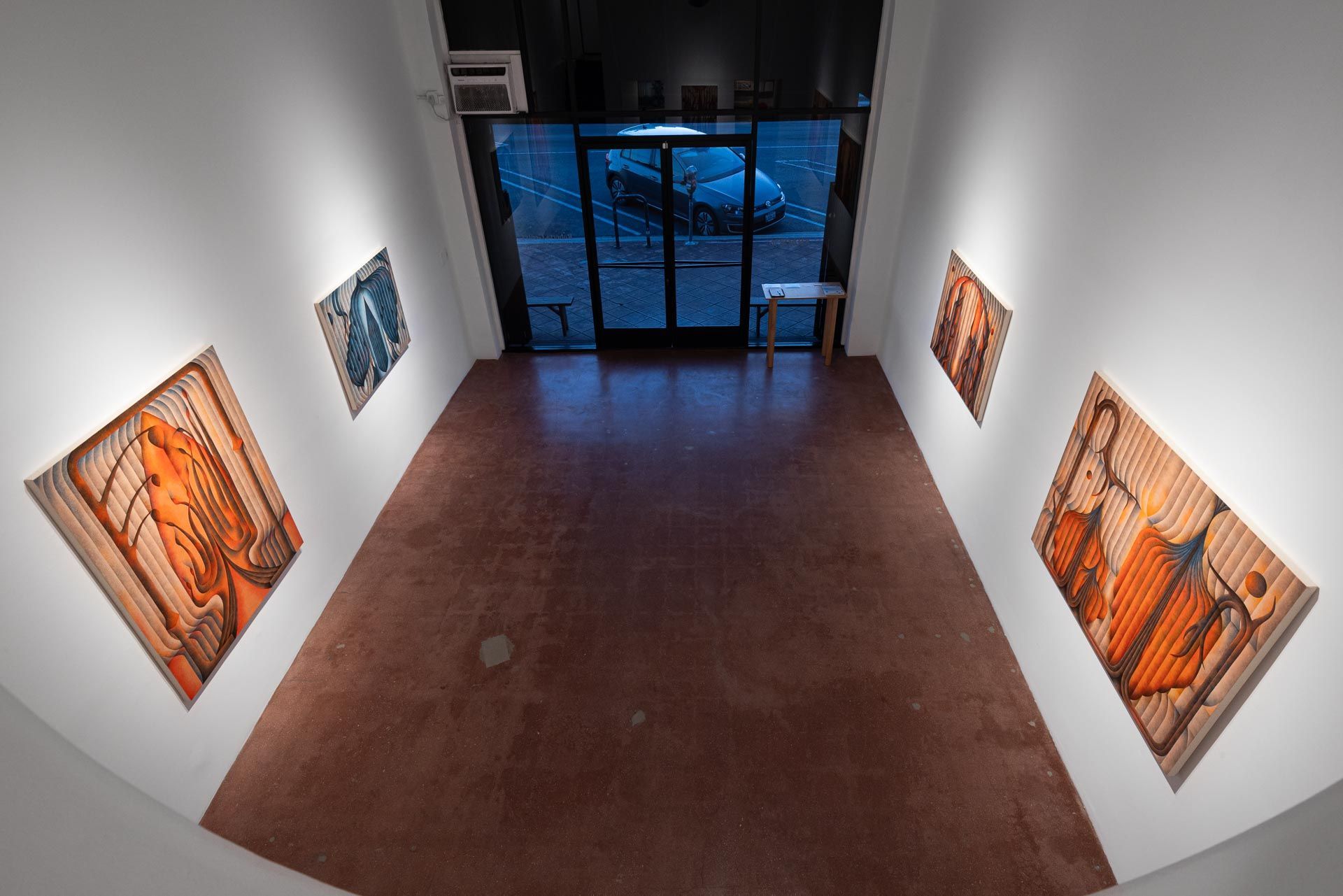High-angle view toward the glass entrance, orange and blue paintings on both walls. Installation view, Roberta Gentry: Blood Orange, Track 16, Los Angeles.