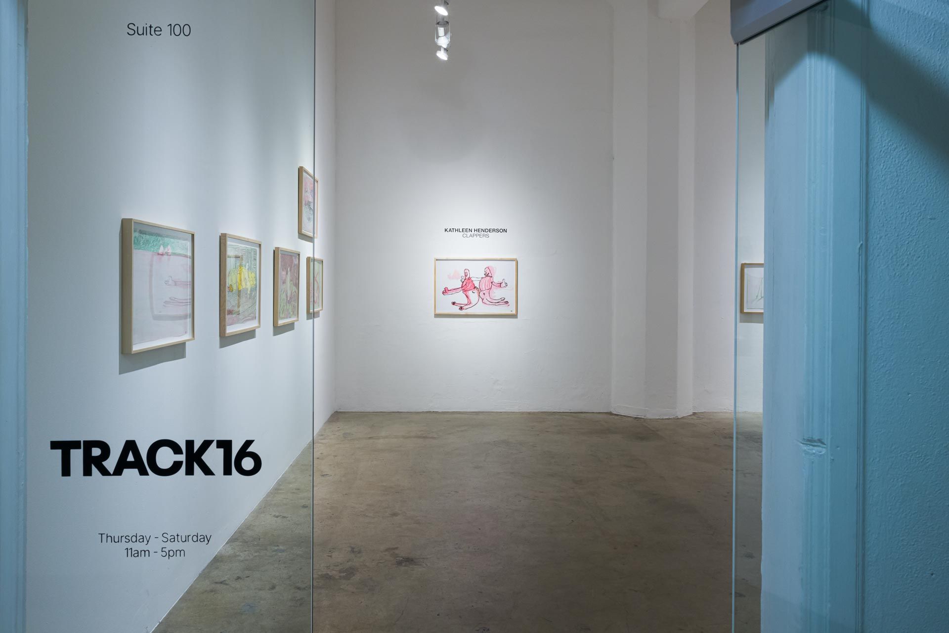 Framed drawings and small wall text on white walls beside a glass wall printed with the TRACK16 logo. Installation view, Kathleen Henderson: Clappers, Track 16.