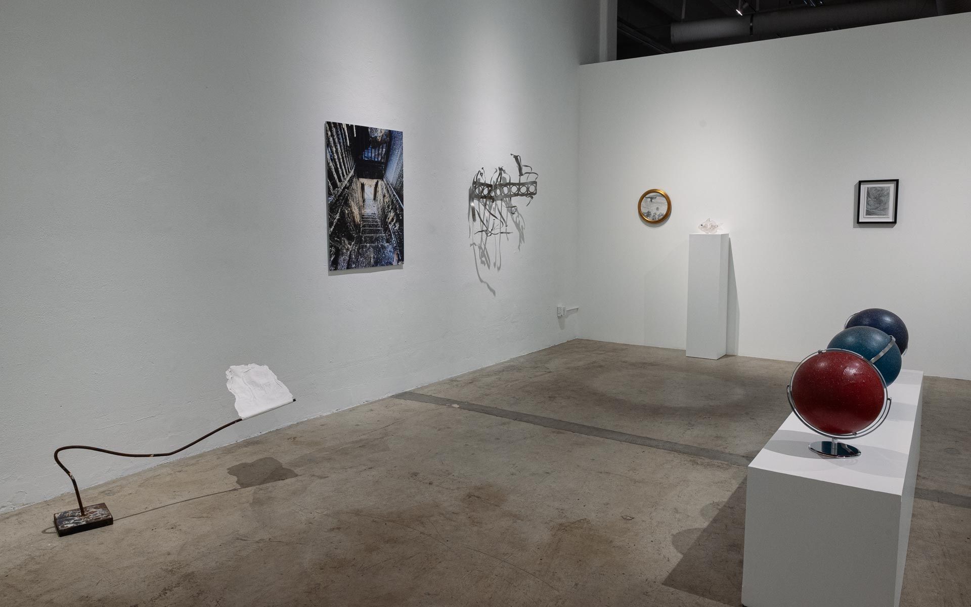 Framed photograph, a wire sculpture and a round framed work on a white wall, a cord on the floor and red and blue globes on a plinth. Installation view, My House Burned Down, Track 16.