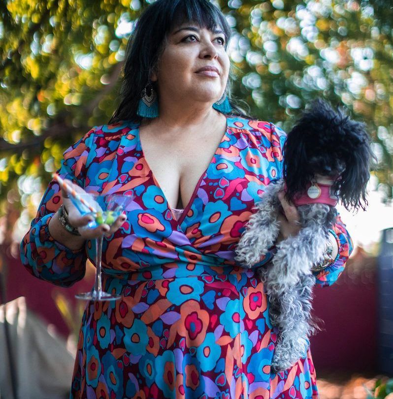 A woman in a floral dress is holding a dog and a martini glass.