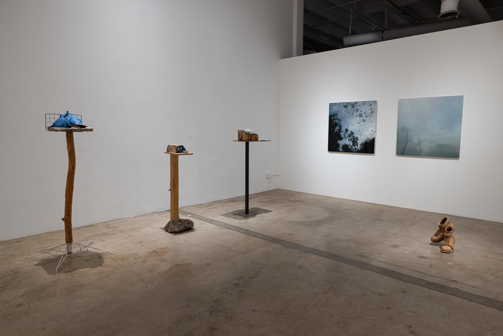 Minimalist art gallery with small sculptures on pedestals and two abstract wall pieces on a concrete floor. VALENCE group art exhibition at Track 16 Downtown Los Angeles featuring sculptures and paintings. Featured artists Azadeh Shladovsky and Daniel Wheeler, Curated by Galia Linn.